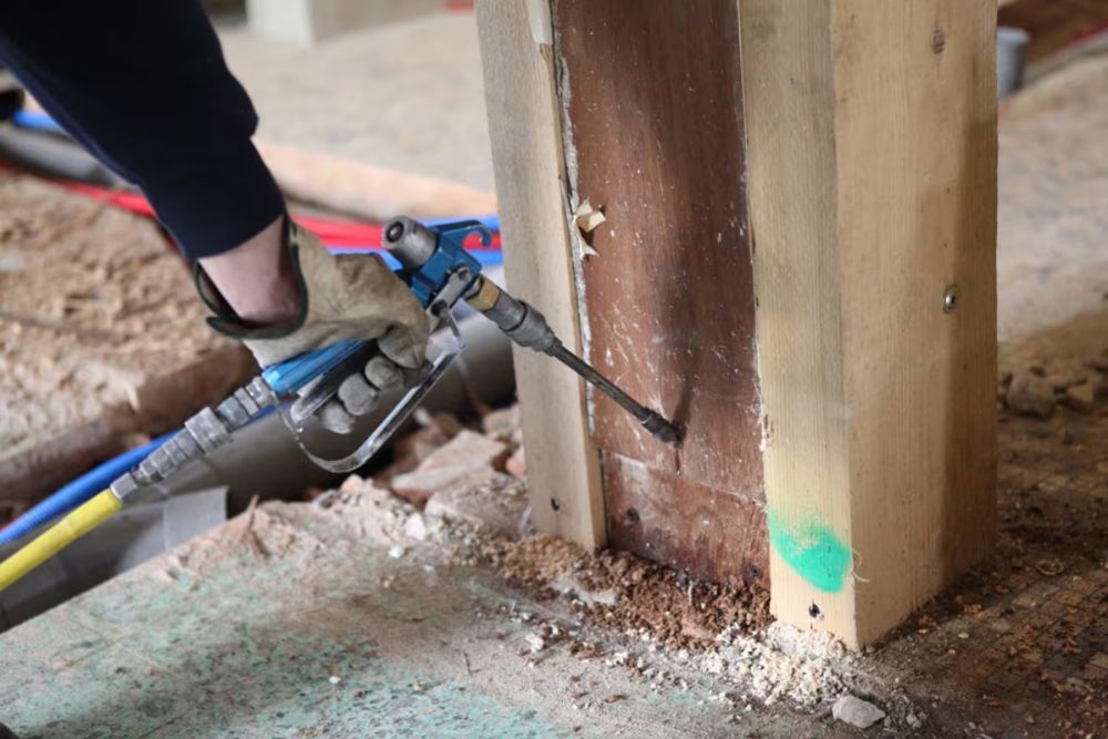 A person uses a power drill to fix a wooden post, related to termite control service in Seattle, WA.